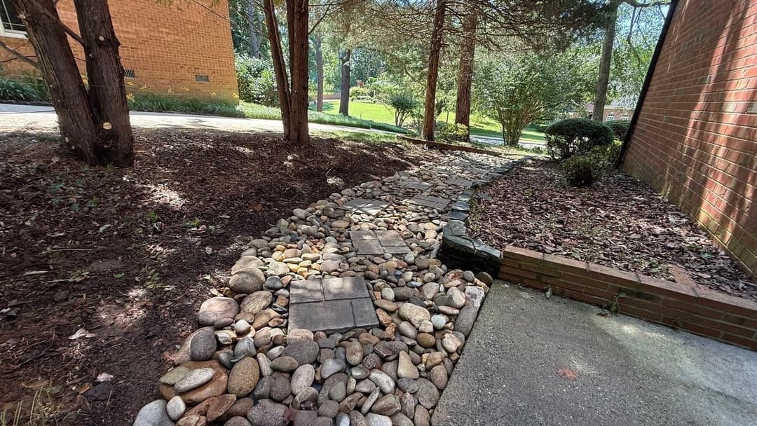 Garden path with stones and pavers surrounded by trees and greenery in a residential setting.