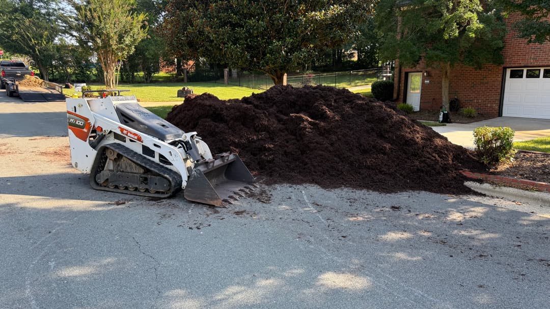 Skid steer loader next to a large pile of mulch on a residential street.