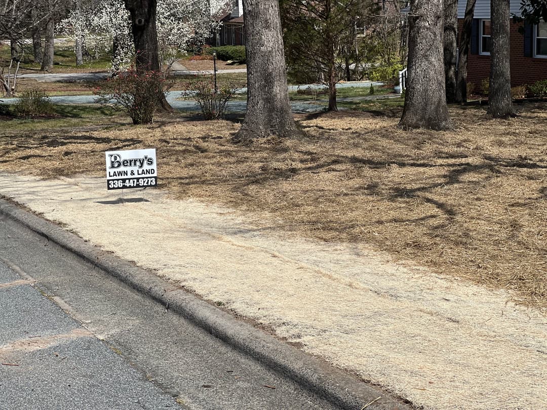 Lawn care sign for Perry's Lawn & Land on a freshly mulched yard with trees nearby.