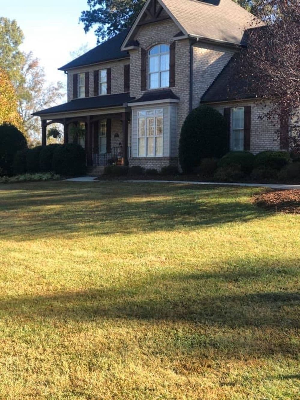 Two-story brick house with a manicured lawn and landscaped garden on a sunny day.