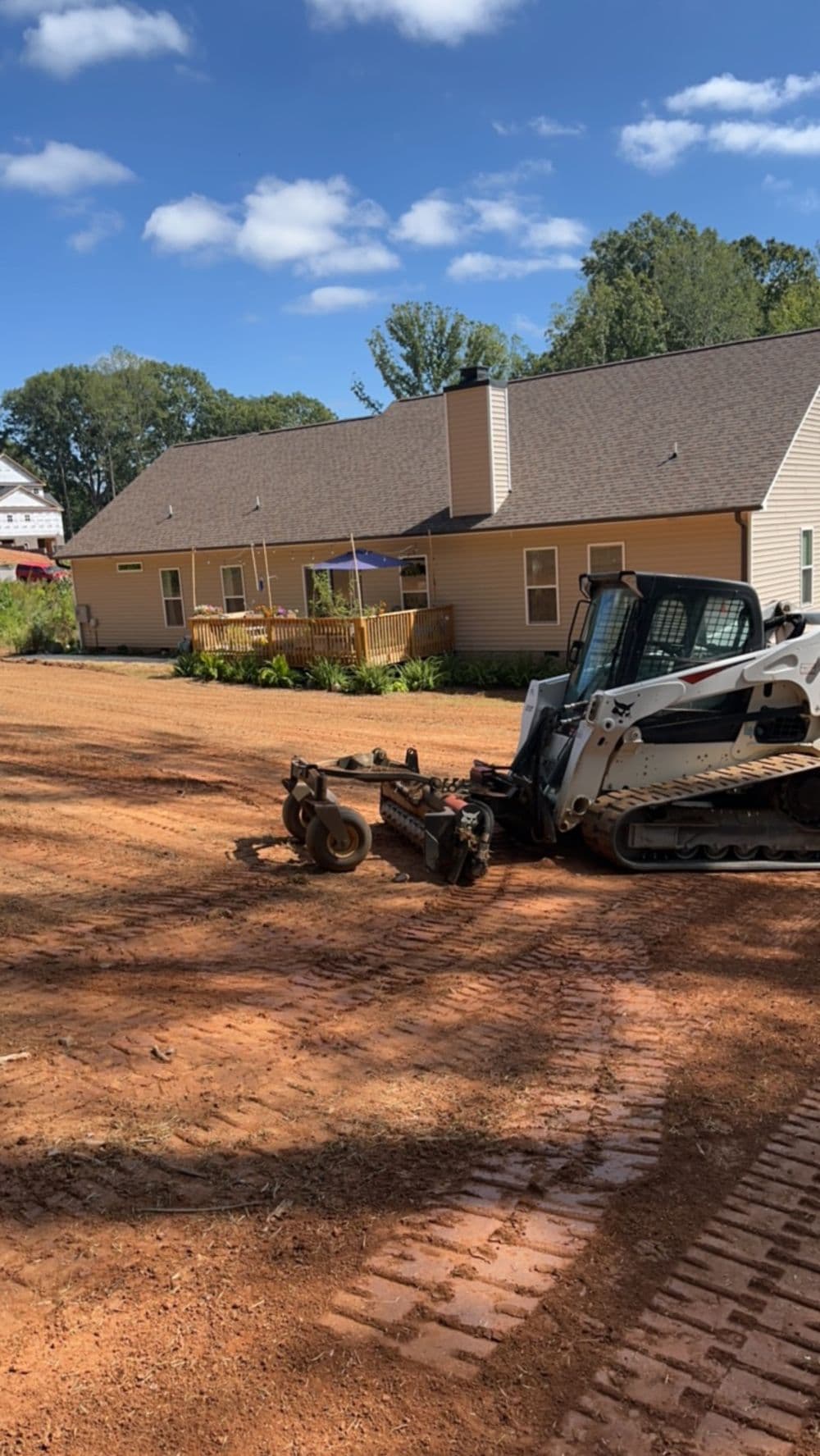Bobcat loader leveling soil in front of a house, preparing for landscaping or construction.