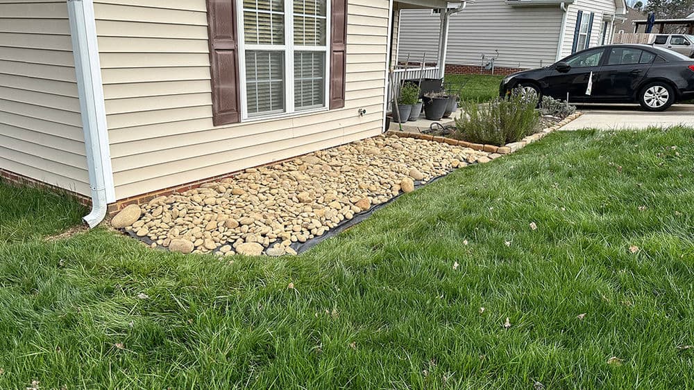 Rocky landscape design featuring a gravel bed beside a house and well-maintained grass.