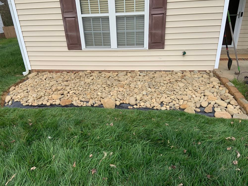 Landscaped area with decorative stones and grass near a house's foundation.