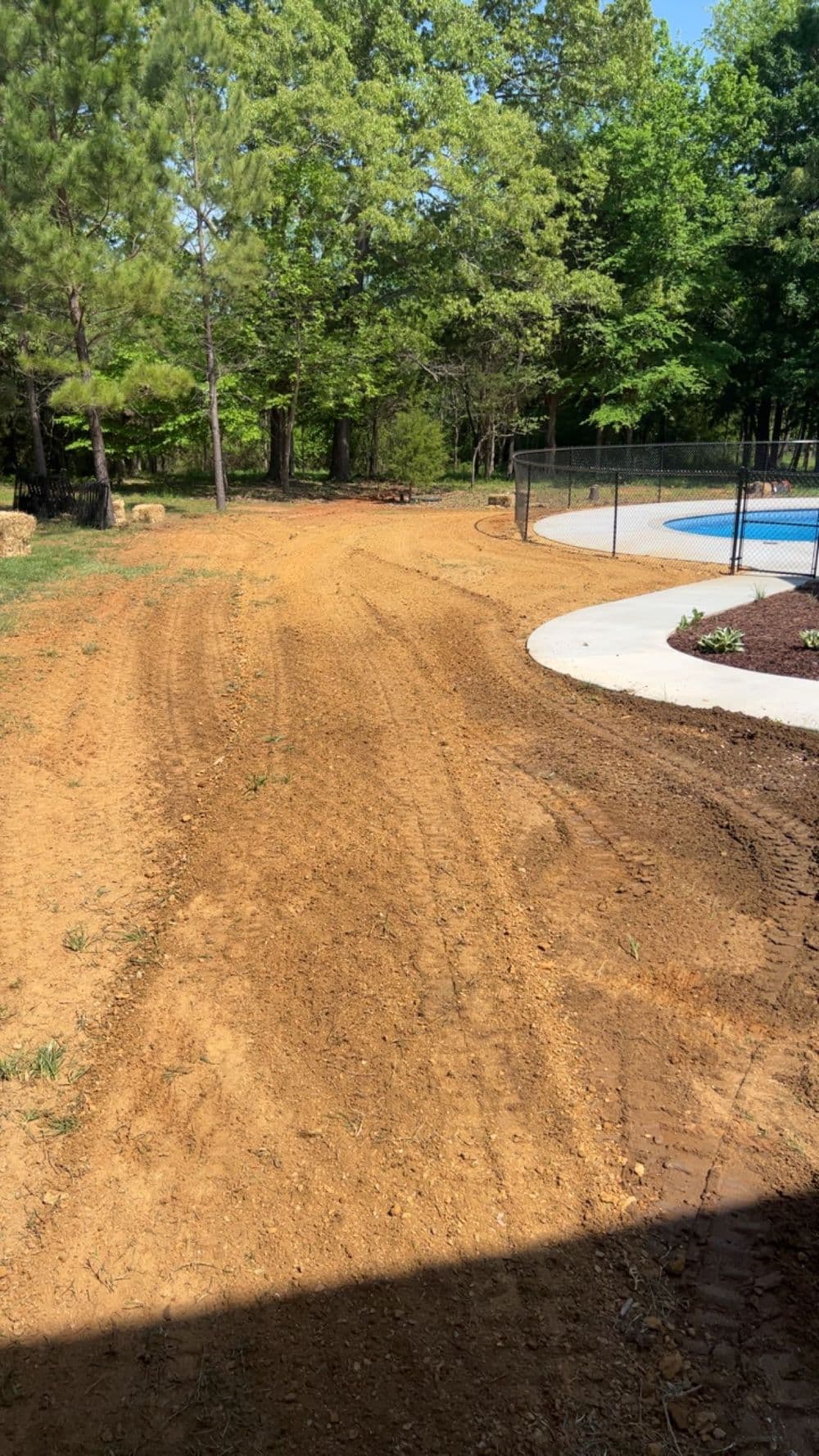 Dirt path leading to a pool area, surrounded by trees and landscaped garden.