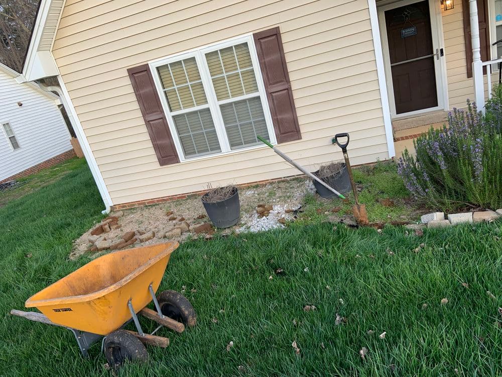 Wheelbarrow and gardening tools outside a house with landscaping in progress.