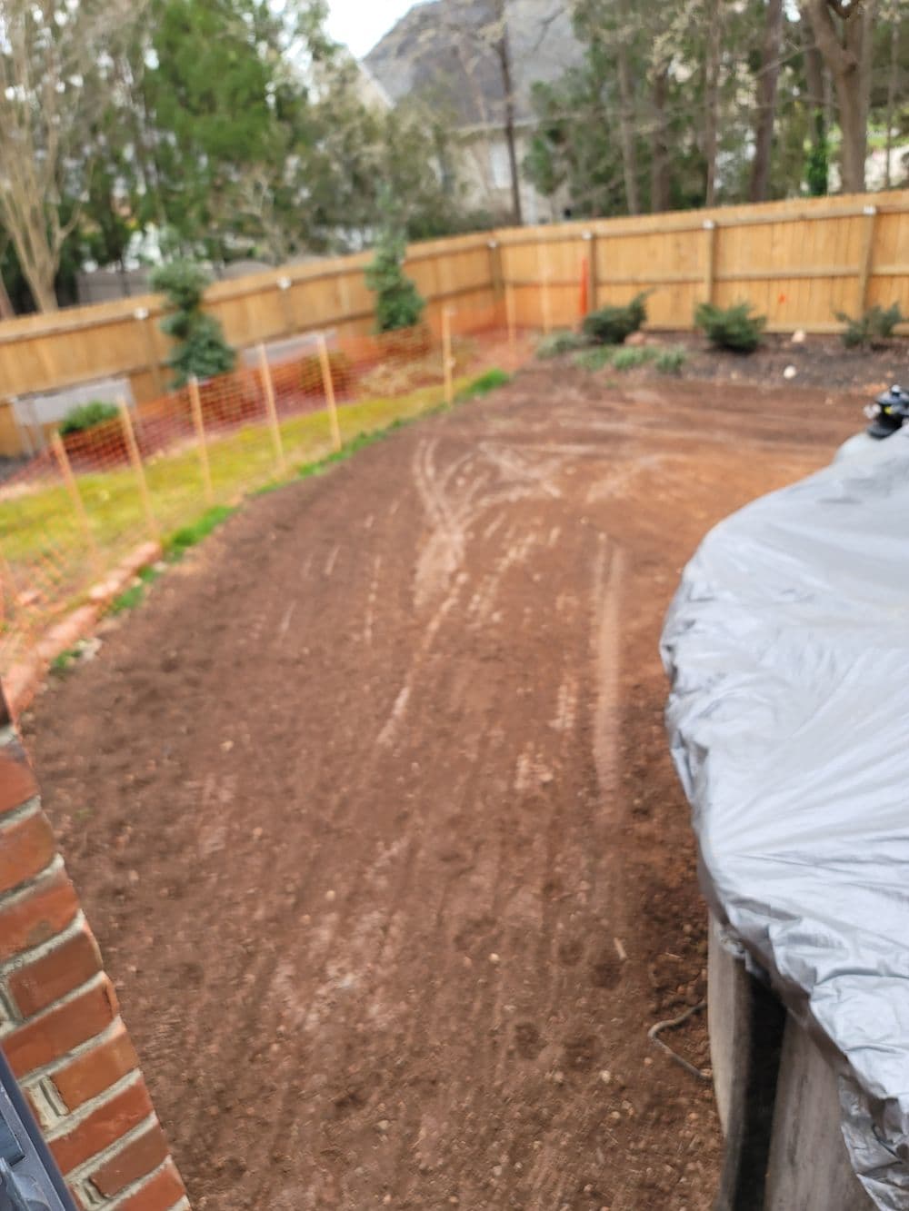 Cleared backyard soil ready for landscaping, surrounded by a wooden fence and trees.