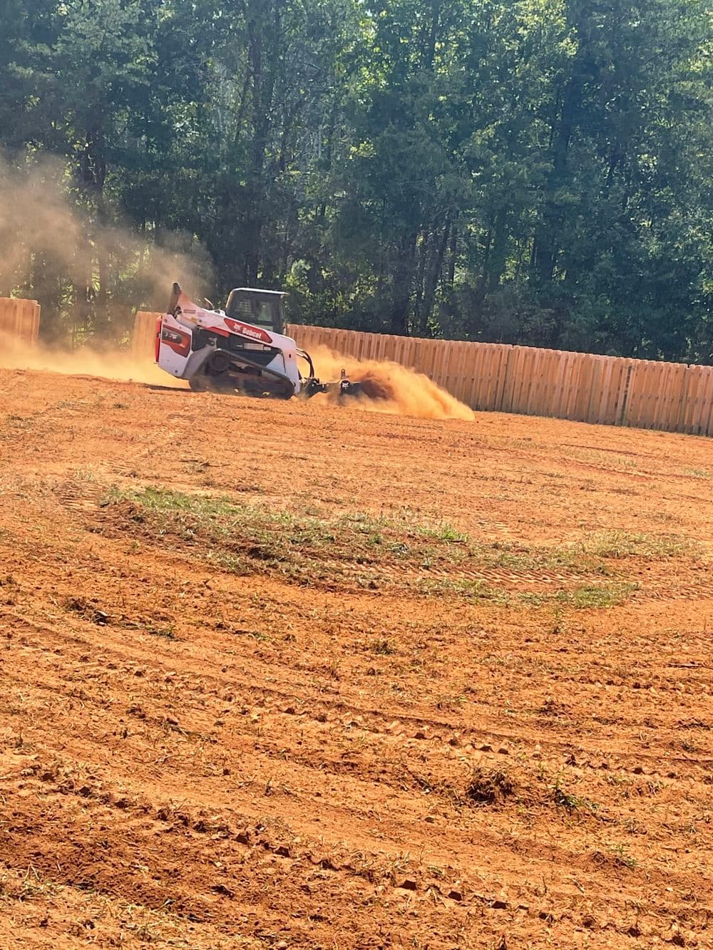 Tractor tilling soil in a field with dust and trees in the background.