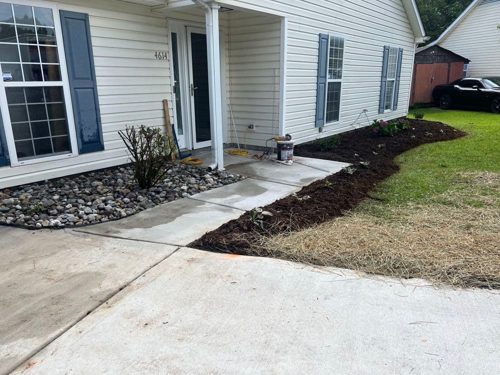 Welcoming entryway with landscaped garden, fresh mulch, and neatly edged concrete walkway.
