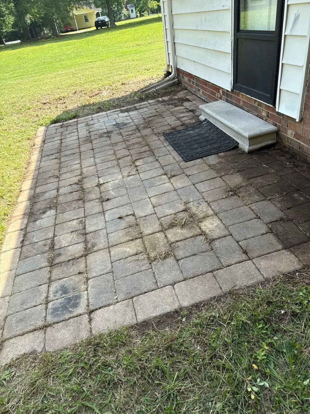 Clean concrete patio with pavers and a doorstep, surrounded by green grass.