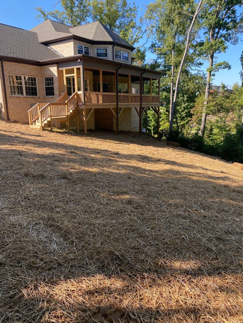 Newly constructed home with a spacious deck surrounded by trees on a sloped lot.