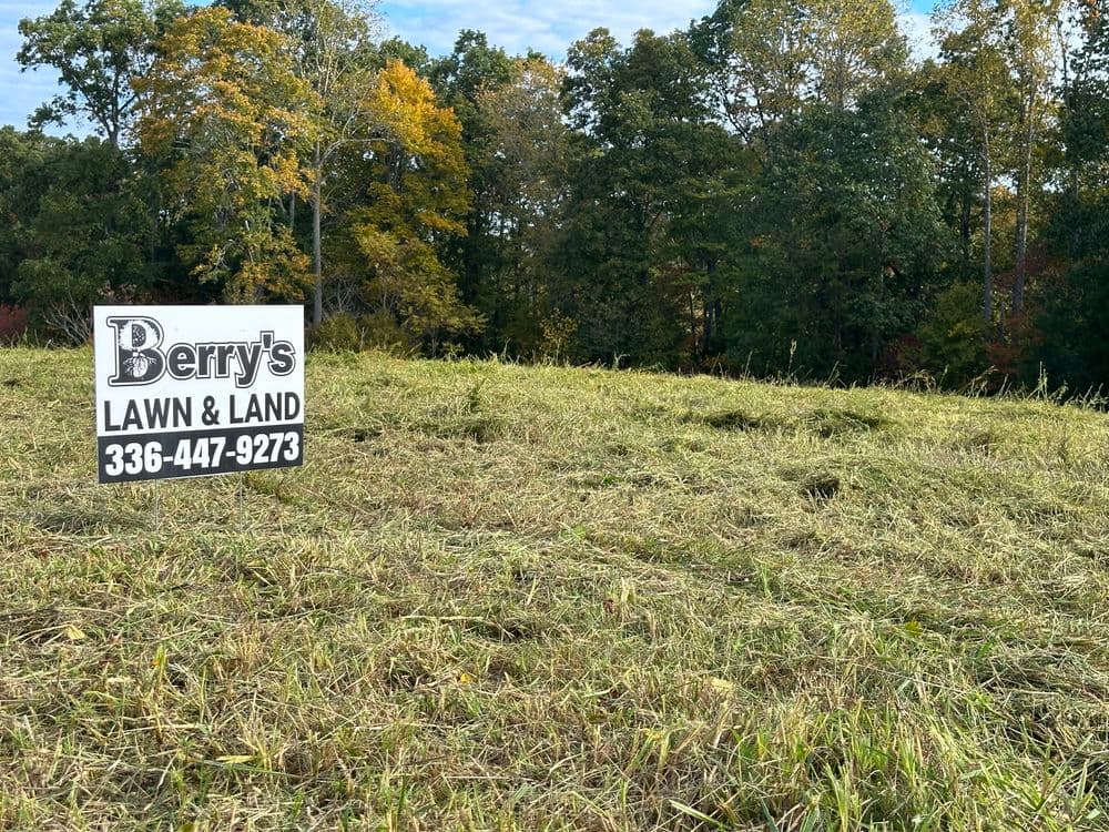 Berry's Lawn & Land sign in a mowed field with trees in the background, phone number 336-447-9273.