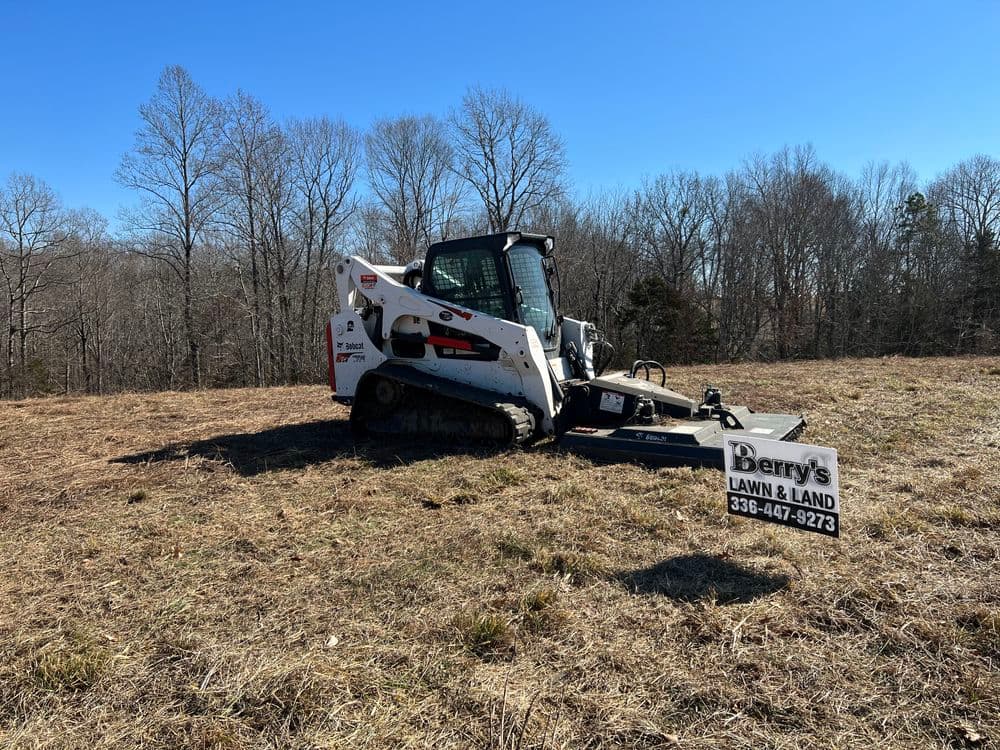 Bobcat skid steer with brush cutter attachment in a grassy field, Derry's Lawn & Land sign visible.