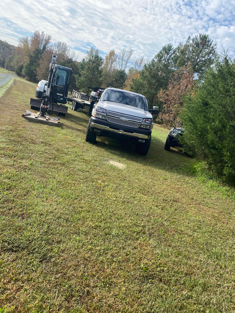 Silver pickup truck parked on grassy area with machinery and trailer in background.
