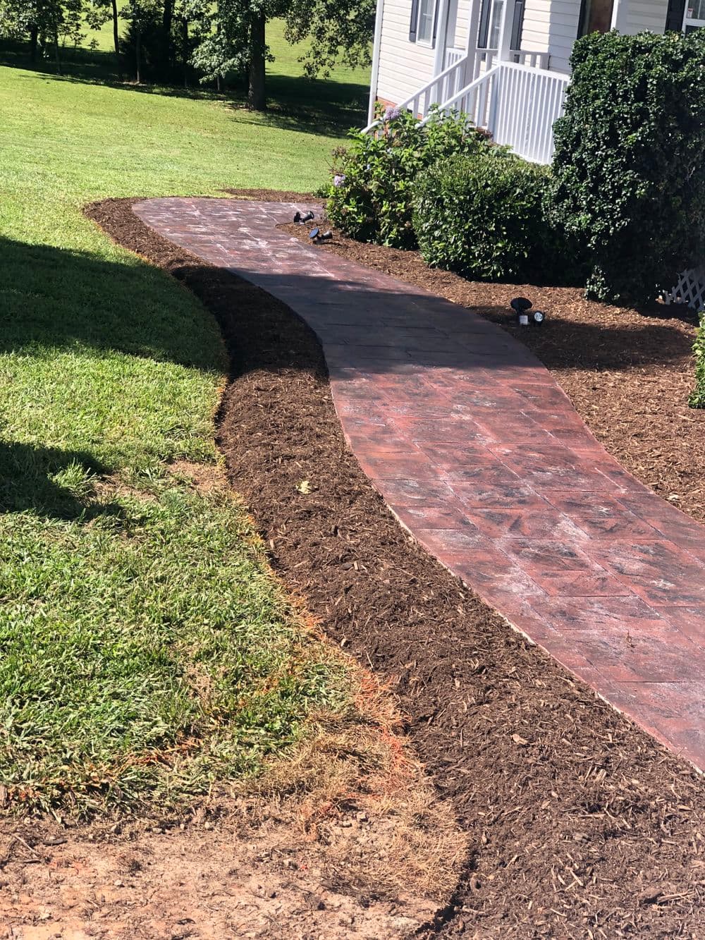 Curved stone pathway beside a house with fresh mulch and green lawn.