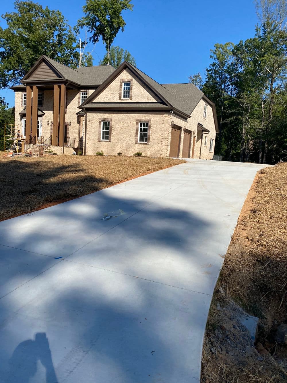 Newly constructed brick home with a concrete driveway and wooded surroundings.