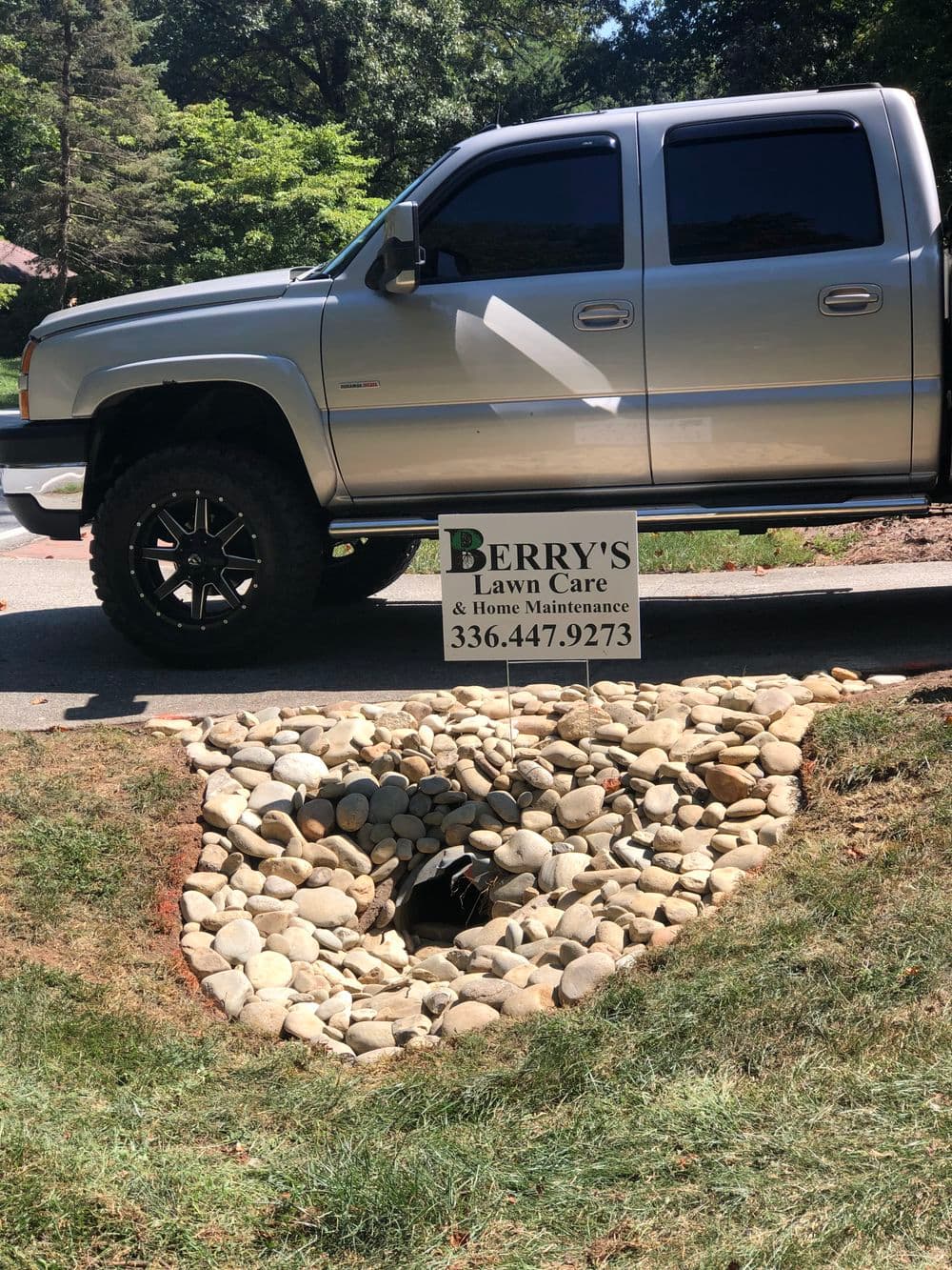 Silver truck parked next to Berry's Lawn Care sign by a stone drainage area.