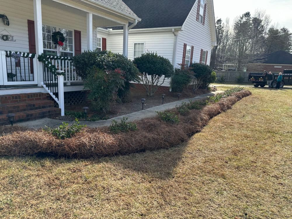 Front yard with neatly arranged shrubs, mulch, and decorative house exterior in winter setting.
